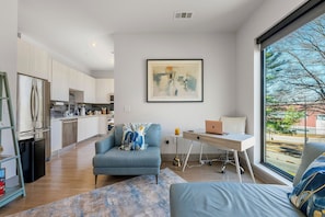 A modern living space with a kitchen, a sofa, a desk with a laptop, and a large window with a view. - Cozy 1-bedroom apartment with Fast WiFi in peaceful Atlanta (Atlanta)