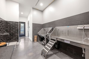 A modern restroom with black tiled walls, a metal sink station, and a caution sign for wet floor. - Cozy 1-bedroom apartment with Fast WiFi in peaceful Atlanta (Atlanta)