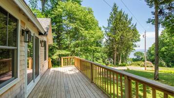 A wooden deck with a railing, overlooking a lush green landscape with trees and a small structure.