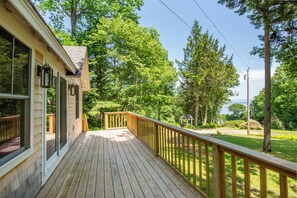 Een houten terras met een balustrade, met uitzicht op een weelderig groen landschap met bomen en een klein gebouw.