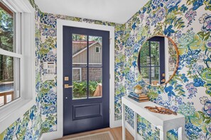 A room with a dark door, a white console table with a mirror, and floral wallpaper. - Charming 2BR Waterfront Cottage on Penobscot Bay located on 20 Private Acres (Northport)
