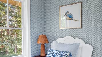 A bedroom with a bed, a framed picture of a bird, a lamp, and a window with a view of trees.