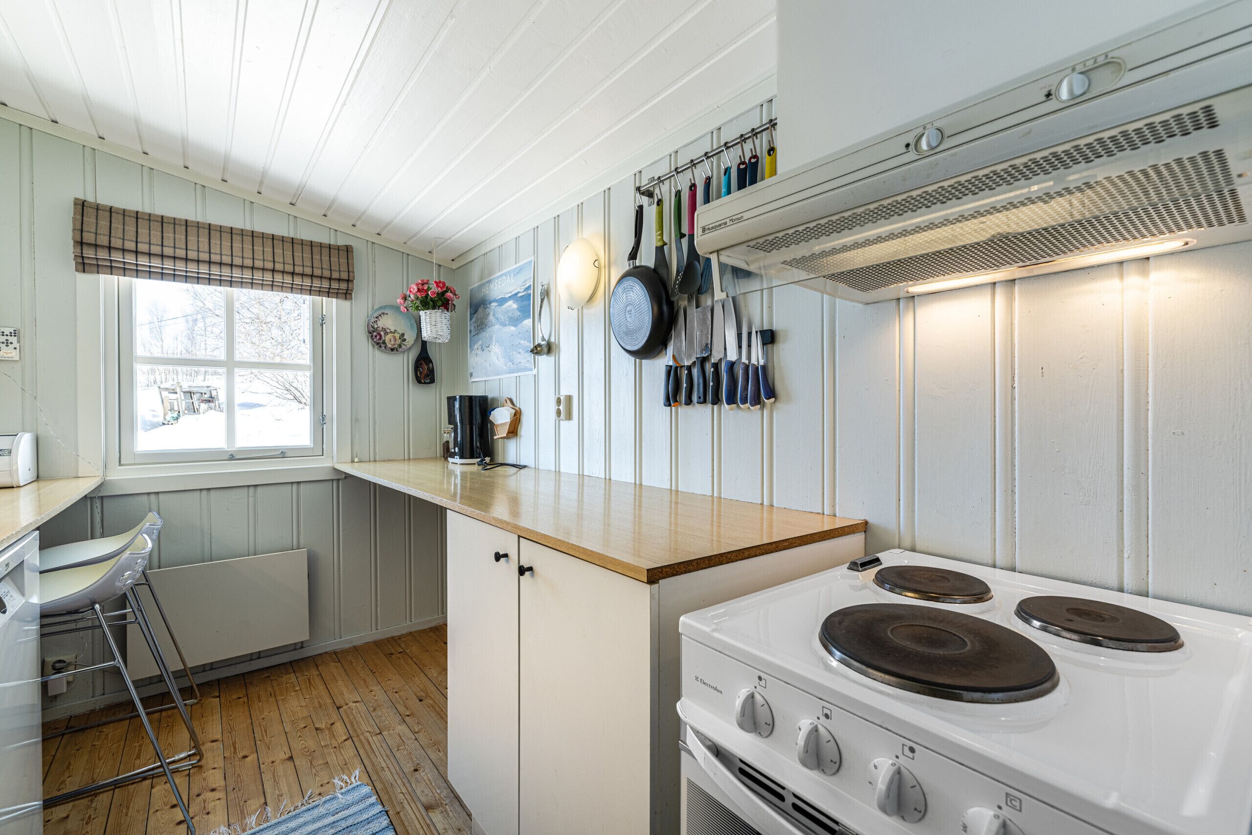 A kitchen with a stove, a sink, and a window with a view of a snowy landscape.