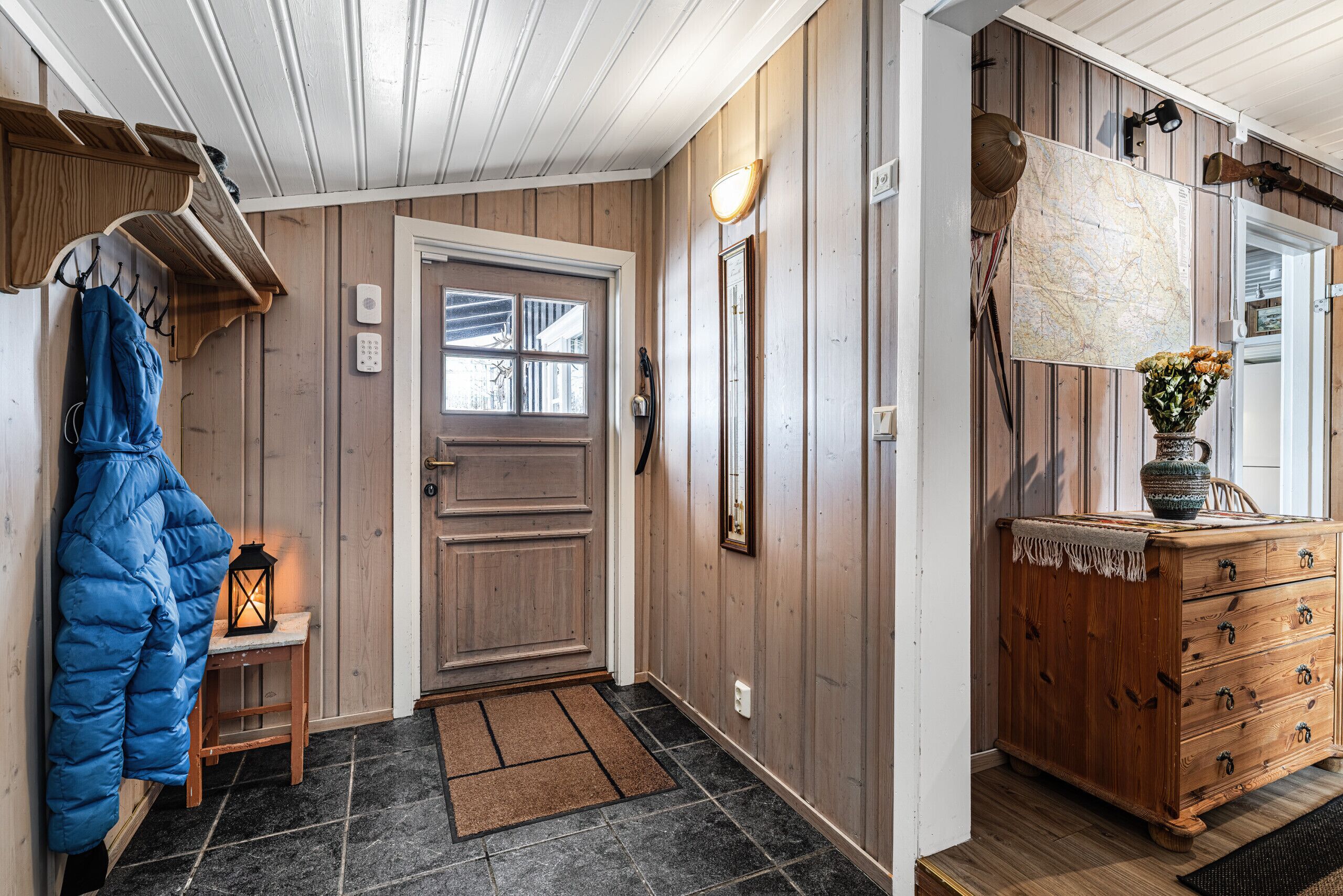 Interior em madeira com porta, um porta-roupas, um banco, cômoda e um mapa na parede.