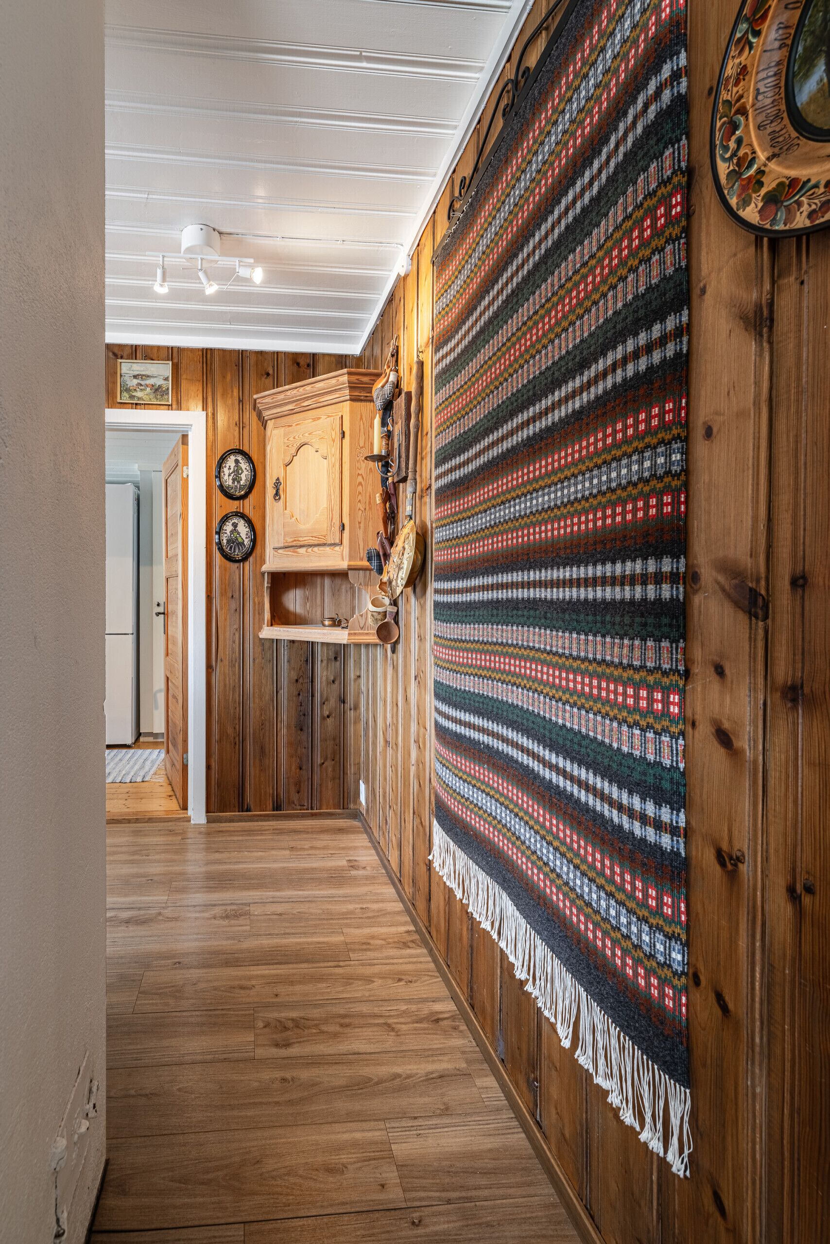 Un pasillo con paredes de madera, un tapete estampado y un mueble de madera.