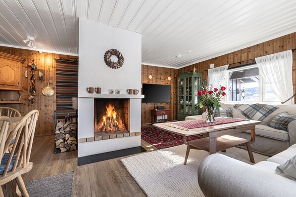 Una sala de estar acogedora con chimenea, paredes de madera, un sofá y una mesa con un jarrón de flores.