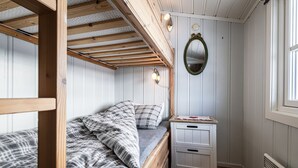 Un lit superposé avec une couverture à carreaux, une table de chevet avec des tiroirs, un miroir fixé au mur et une fenêtre donnant sur un paysage.