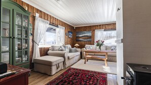 Un salon chaleureux avec un canapé, un pouf et une table basse. On y trouve un meuble vert avec des portes en verre et une cheminée.