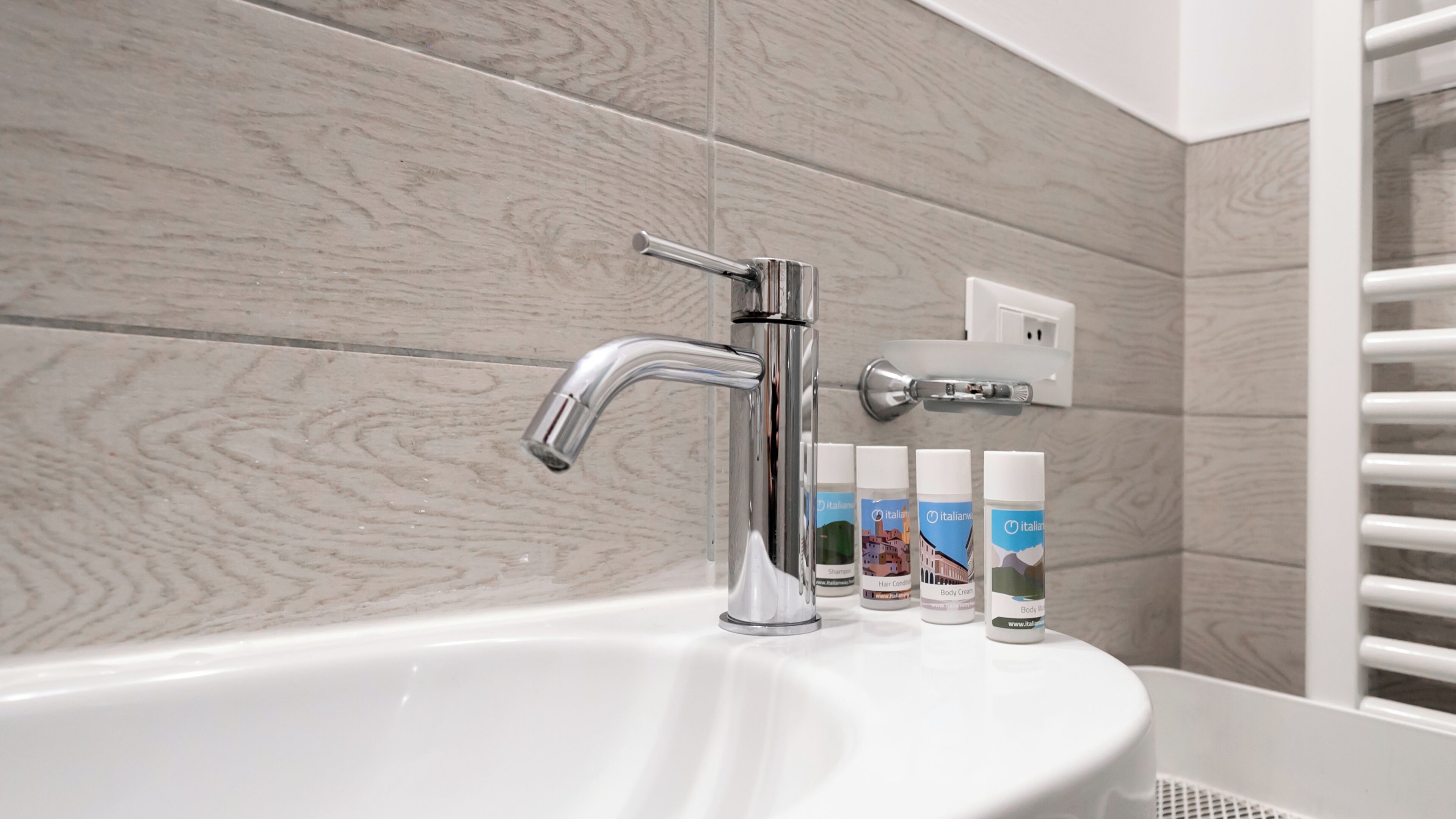 A bathroom with a white sink, chrome faucet, and three bottles of Italian body care products.