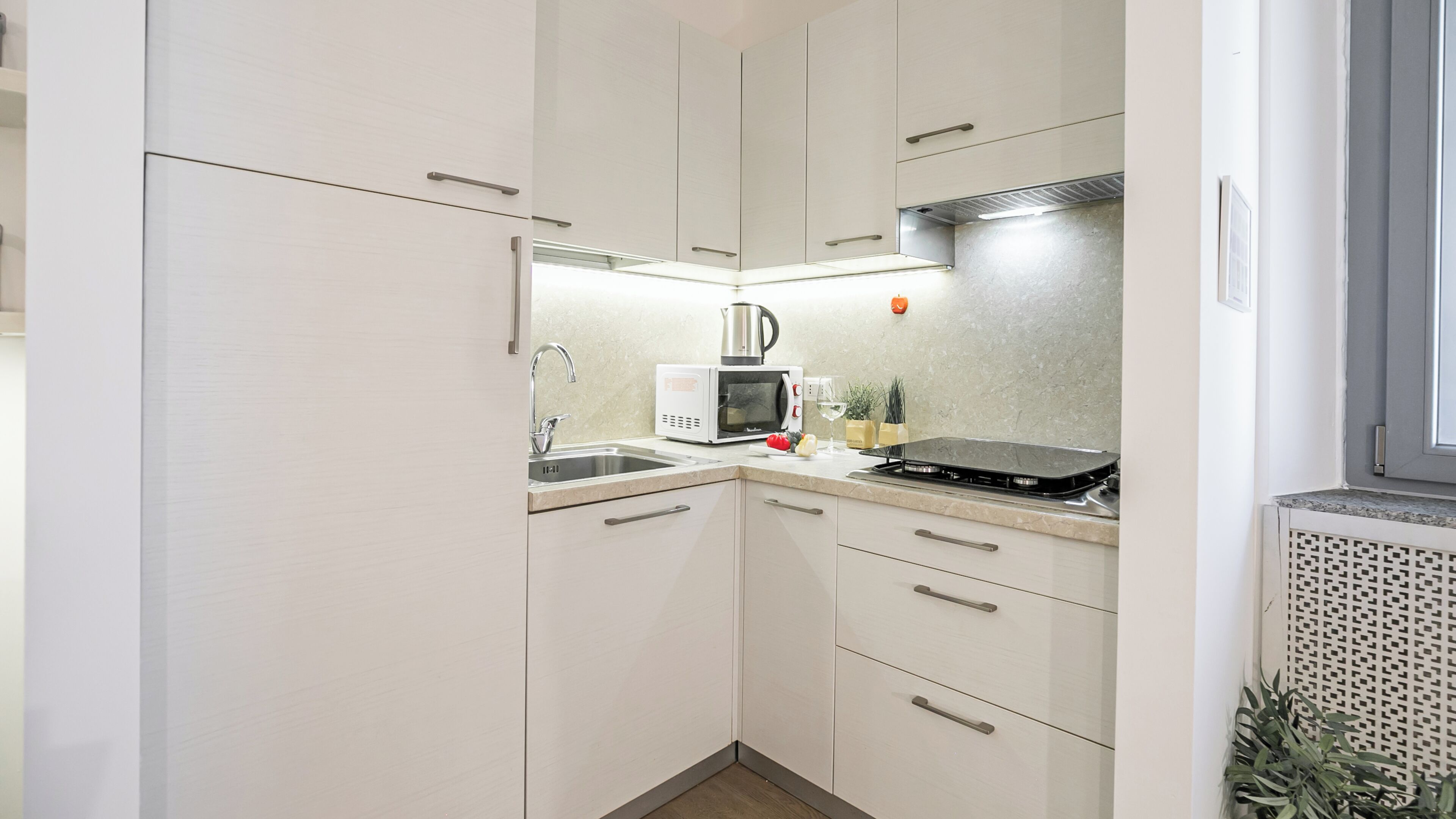 A compact kitchen with white cabinets, a sink, a microwave, and a gas stove.