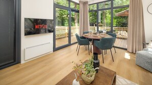 A modern living room with a dining area, large windows, a TV, and a wooden deck.
