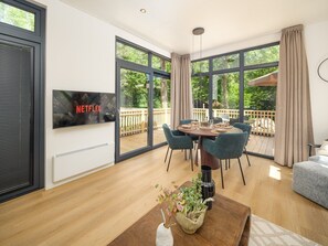 Una sala de estar moderna con comedor, ventanas amplias, televisor y terraza de madera.