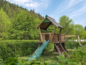 A wooden play structure with a slide and swings in a garden.