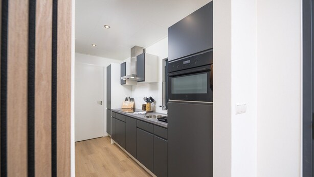 A modern kitchen with dark cabinetry, a built-in oven, and a stainless steel range hood.