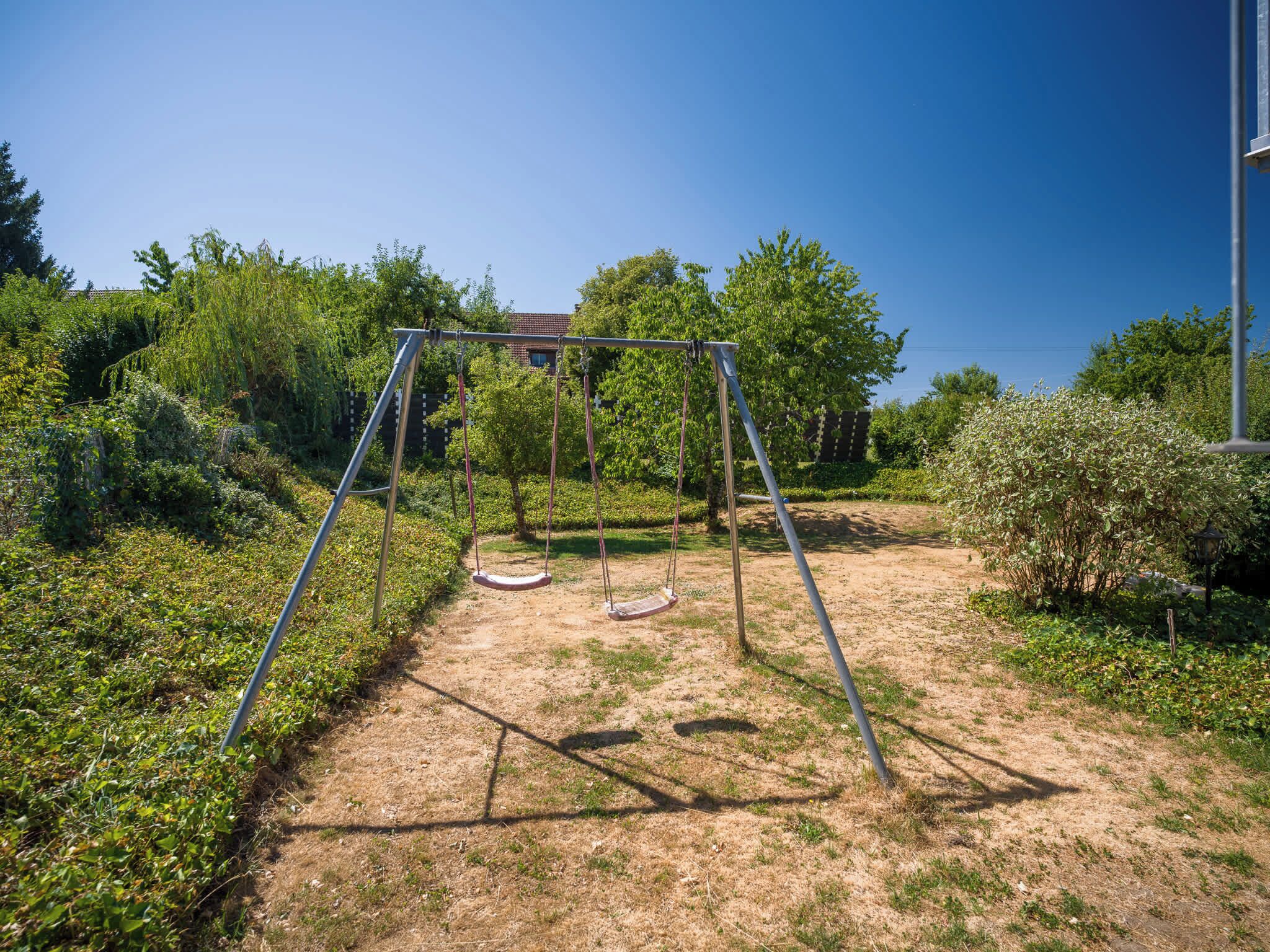 Eine Schaukelanlage in einer grünen Wiese mit Bäumen und einem Gebäude im Hintergrund.
