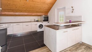 A modern kitchen with a wooden ceiling, a built-in oven, a washing machine, and a small window. - Central Apartment near Bern, Parking & Balcony (Ried bei Kerzers)