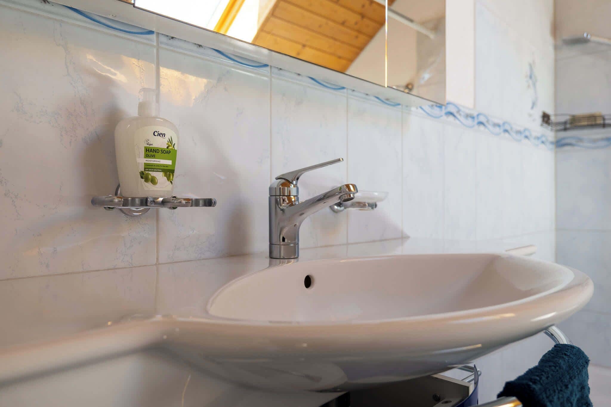 A bathroom with a white sink, a faucet, and a soap dispenser on the wall.
