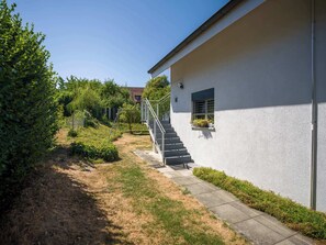 En moderne bygning med hvide facader, en sti af beton og en metal trappe, der fører op til et vindue med plantekasser.