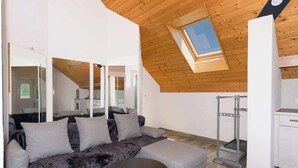 A modern living space with a sloped ceiling, a built-in kitchen, a grey sofa, and a small round table. - Central Apartment near Bern, Parking & Balcony (Ried bei Kerzers)