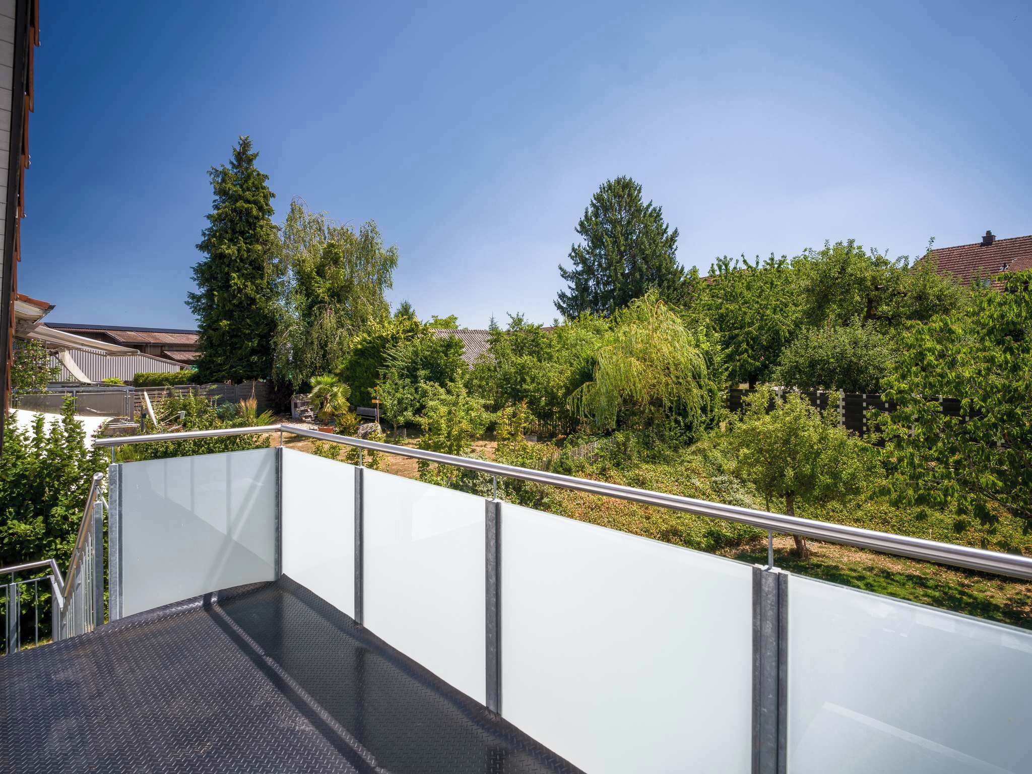Une terrasse sur le toit, dotée d’une rambarde en métal, entourée d’une végétation luxuriante et d’arbres.