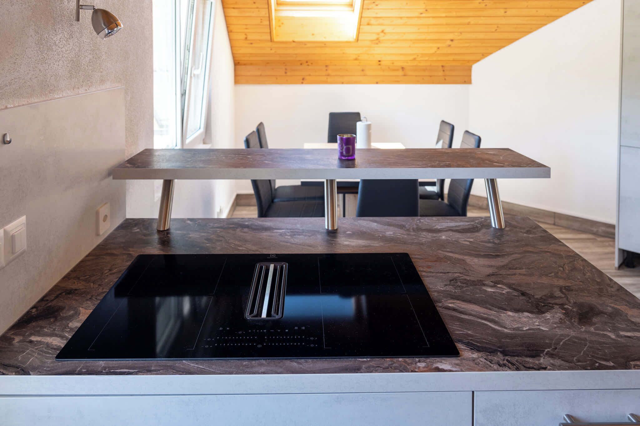 A modern kitchen with a built-in induction cooktop, a wooden dining table, and a high ceiling with a skylight.