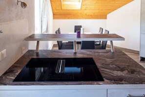 Et moderne køkken med en integreret induktionskogeplade, et træspisebord og et højt loft med ovenlys.