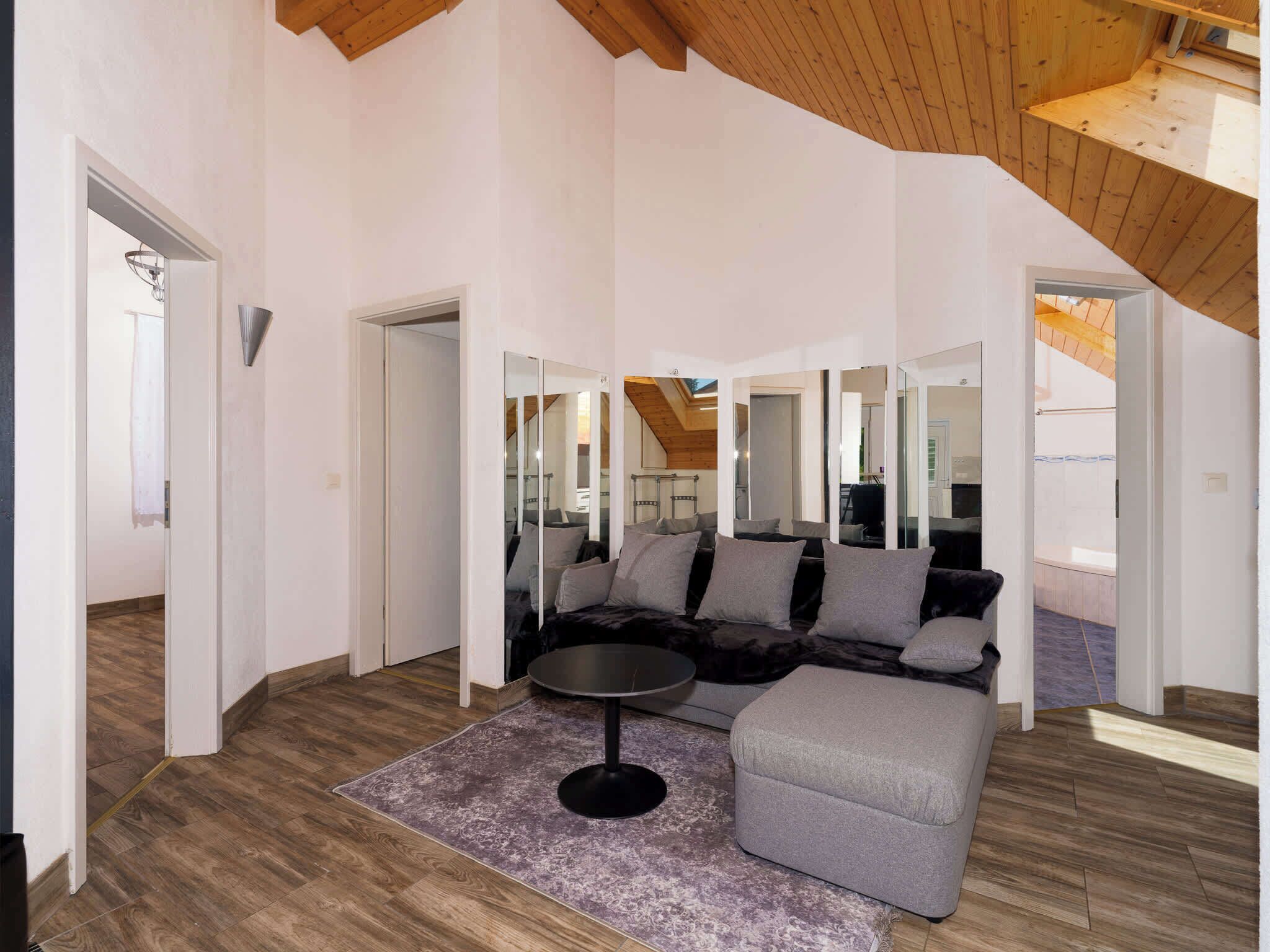 A spacious living area with a wooden ceiling, a grey sofa, a round coffee table, and a purple rug.