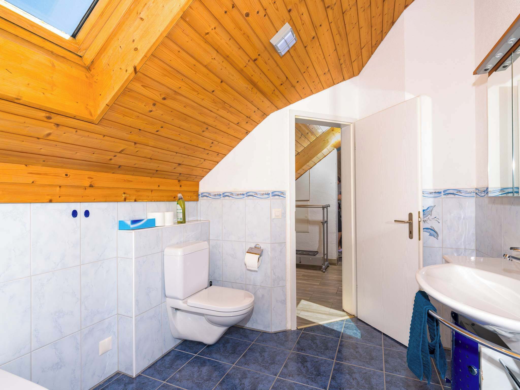 Un baño con tragaluz, inodoro blanco, piso de azulejos azules y un lavabo con espejo.