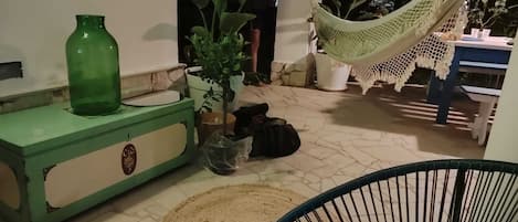 Uma área de pátio com um armário verde, um tapete tecido, uma rede e plantas em vasos.