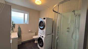 A compact bathroom with a washing machine, toilet, and glass-enclosed shower.