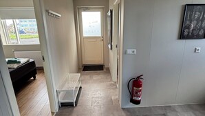 Un passadís amb una porta que dona a un dormitori, un extintor fixat a la paret i una finestra amb vista a l'exterior.