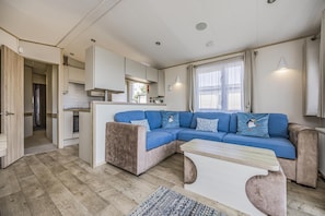 A modern, compact living space with a sofa set, a dining area, and a kitchen. - Lovely Home in Church Farm Haven Park - Pass the Keys (Pagham)