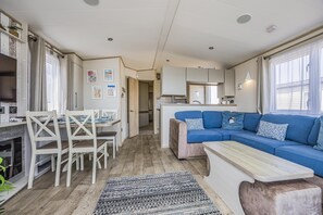 A compact living space with a dining area, kitchenette, and a sofa with decorative pillows. - Lovely Home in Church Farm Haven Park - Pass the Keys (Pagham)