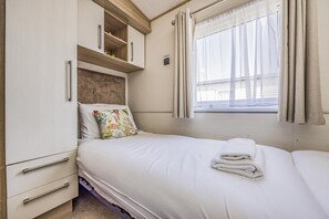 A bedroom with a bed, a nightstand, a dresser, and a window with curtains. - Lovely Home in Church Farm Haven Park - Pass the Keys (Pagham)