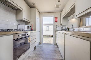 A compact kitchen with a microwave, stove, oven, and a sink. - Lovely Home in Church Farm Haven Park - Pass the Keys (Pagham)