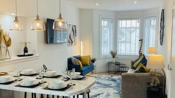 A well-lit dining area with a table set for a meal, a blue sofa with cushions, and a small side table with a lamp.