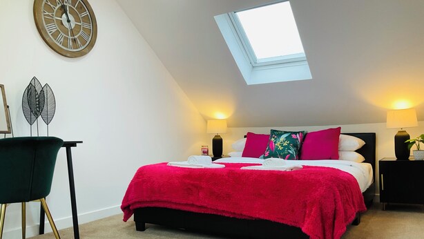 A bedroom with a skylight, a bed with a red blanket, two bedside lamps, and a chair. - Prestwick - 4 bedroom house, off-street parking (Prestwick)