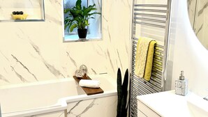 A bathroom with a bathtub, a toilet, a sink, a mirror, and a window with a plant. - Prestwick - 4 bedroom house, off-street parking (Prestwick)