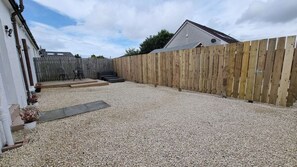 A backyard with a gravel surface, a wooden fence, and a house with a sloped roof.