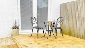 An outdoor patio with a wooden deck, two metal chairs, a table, and a potted plant. - Prestwick - 4 bedroom house, off-street parking (Prestwick)