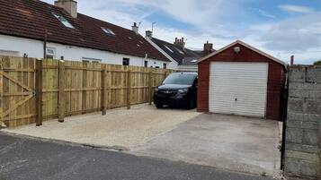 A residential garage with a car parked inside, a wooden fence, and a house in the background.