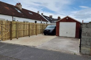 A residential garage with a car parked inside, a wooden fence, and a house in the background.