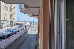 A balcony with a view of a street, parked cars, and a beach in the distance. - Mare e Conchiglie (Albenga)