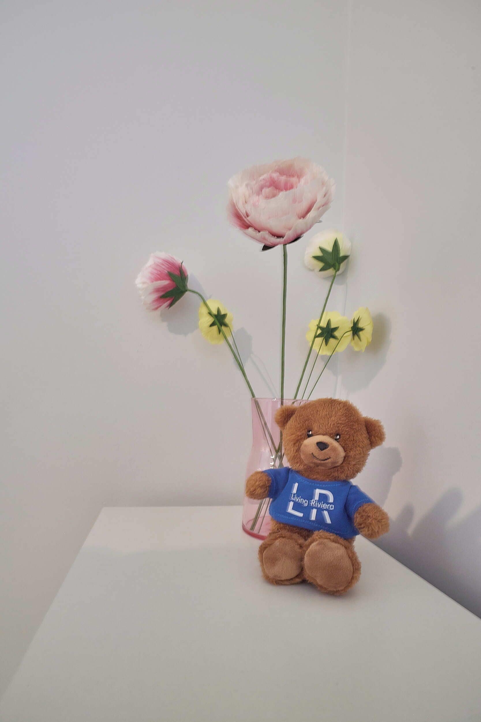 A brown teddy bear with a blue shirt holding a vase with flowers.