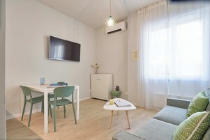 A compact living space with a dining area, a sofa, a TV, and a window with sheer curtains.