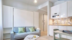A modern, compact living space with a sofa, a small table, and a kitchenette. - Mare e Conchiglie (Albenga)