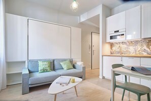 A modern, compact living space with a sofa, a small table, and a kitchenette. - Mare e Conchiglie (Albenga)
