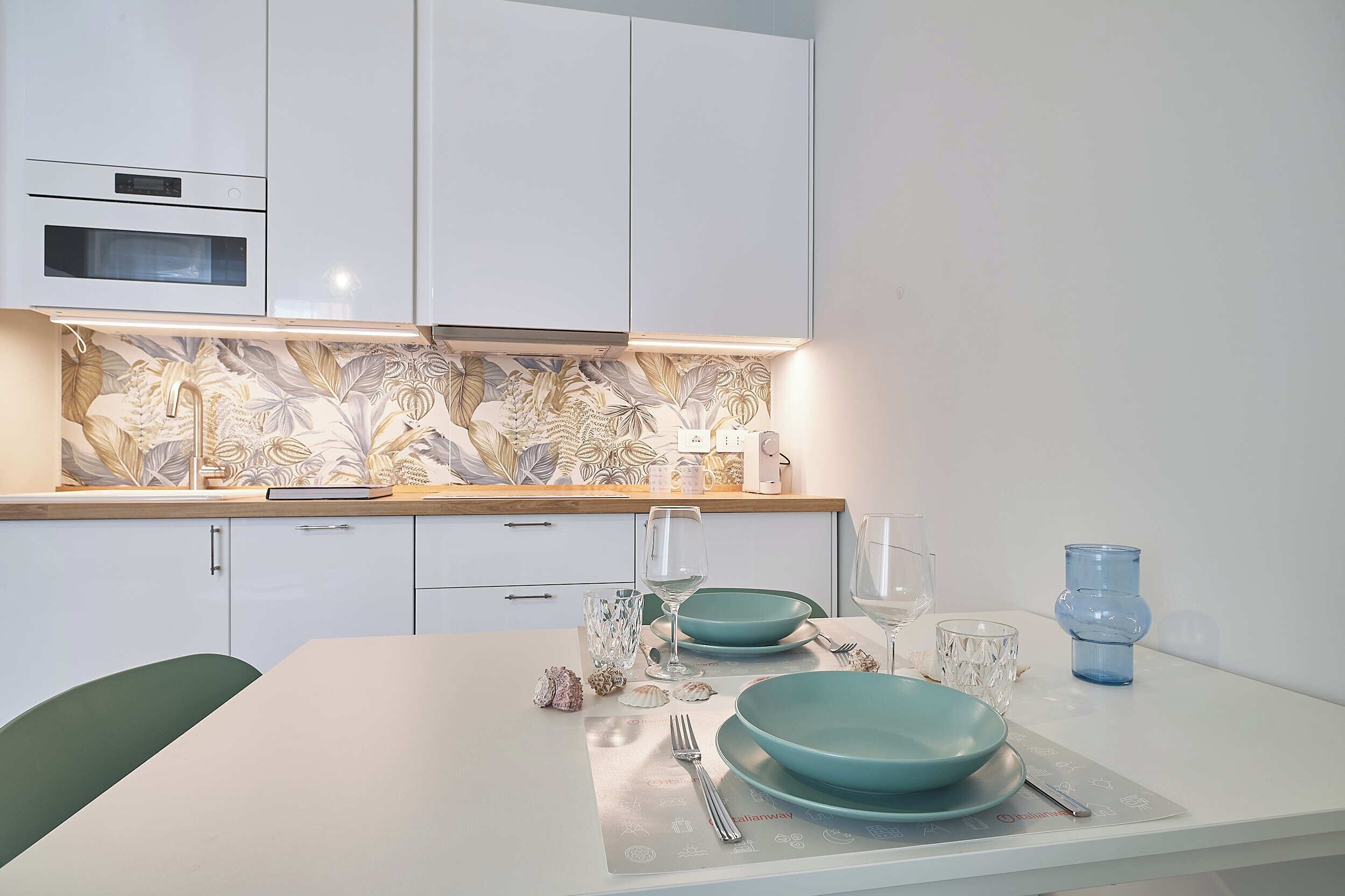 A modern kitchen with white cabinets, a patterned backsplash, and a dining area with a table set for two.