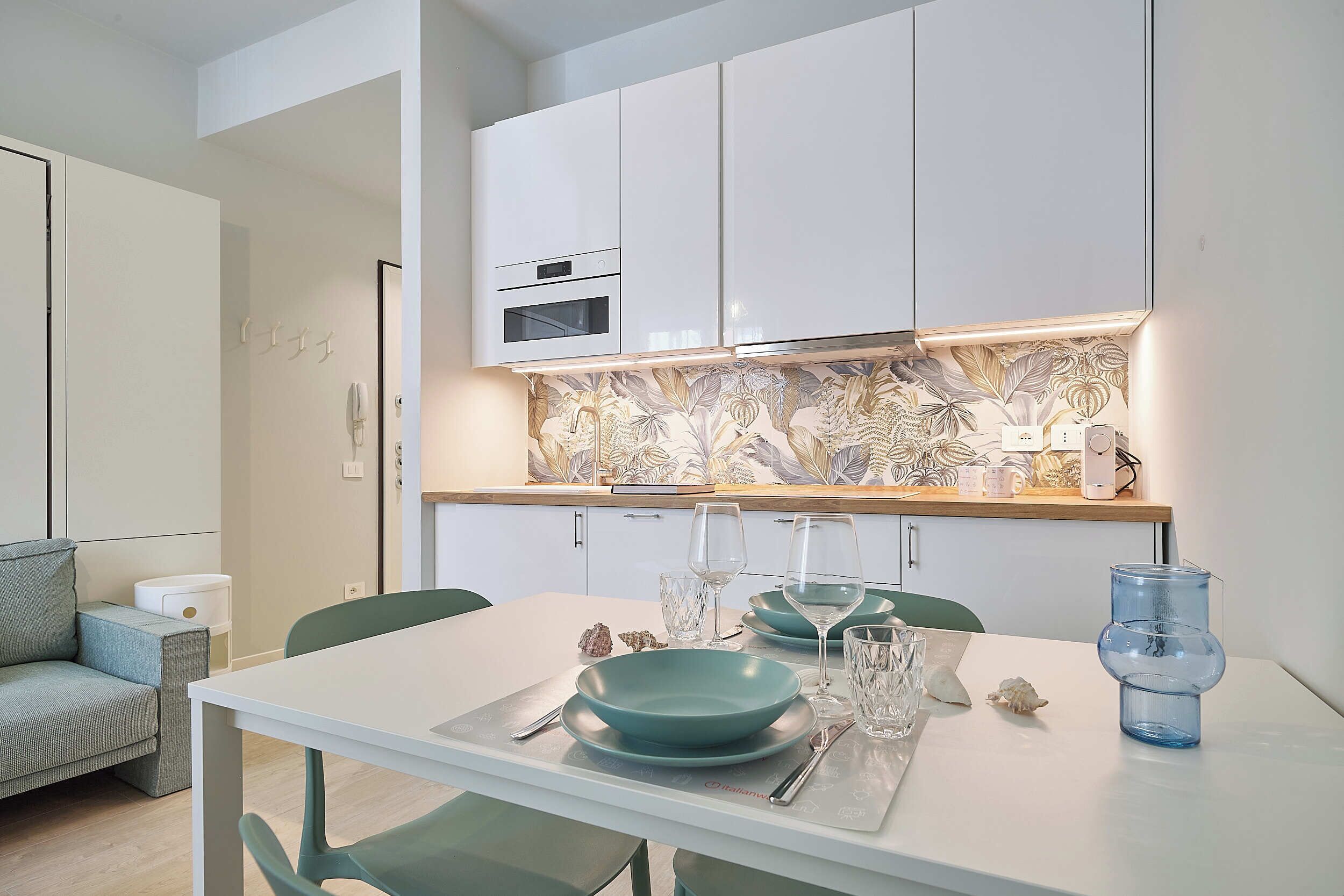 Une cuisine moderne avec des armoires blanches, un four encastré et un pare-feu décoré d’un motif floral.