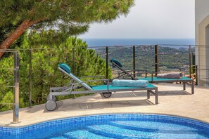 Ein Poolbereich mit Liegestühlen und Blick auf das Meer.